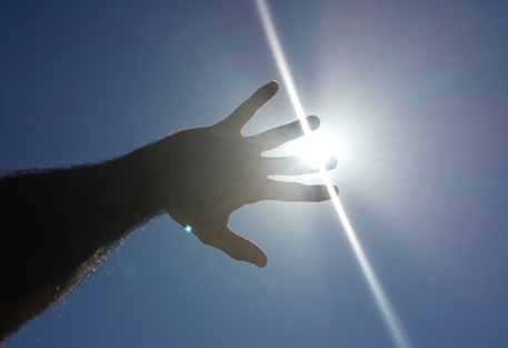 Eine Hand die in den Himmel gestreckt wird und die Sonne verdeckt.